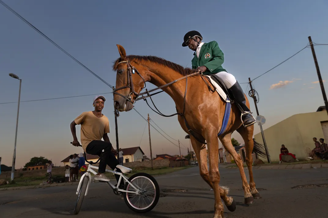 Mafokate chats with a local BMX rider, who playfully circles him and shows off his stunts, on an afternoon ride through the streets of Soweto.