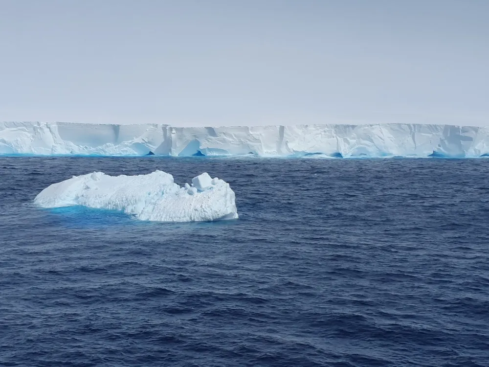 A small iceberg drifts in the ocean in front of a larger one